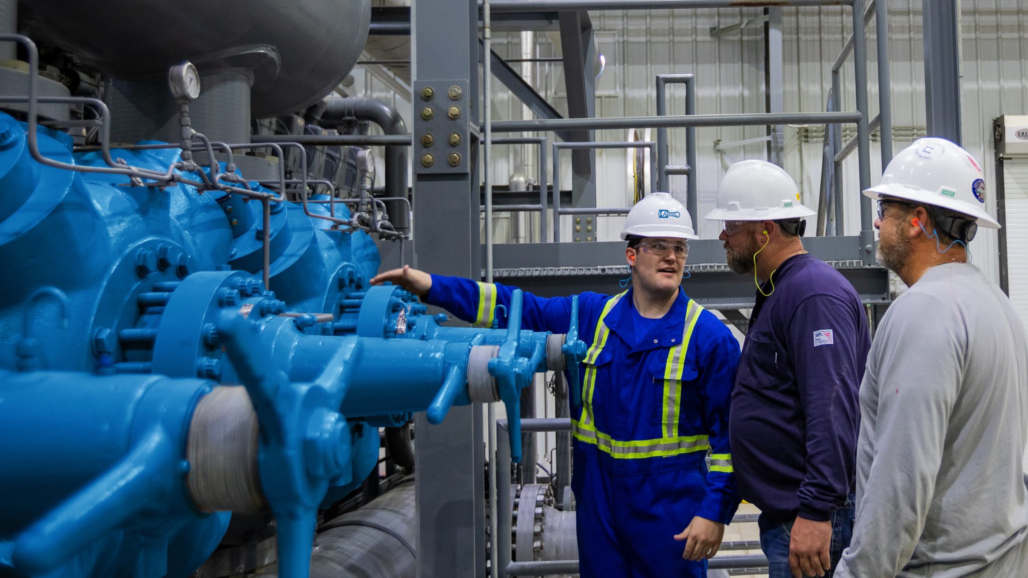 Ariel Field Tech gesturing to a compressor while speaking to a station mechanic and supervisor at Rover Pipeline