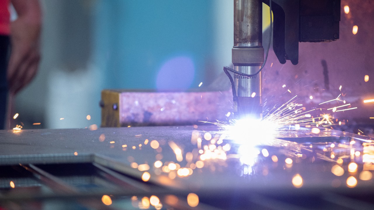 Detail of a plasma cutter cutting a sheet of steel while emitting sparks and bright light